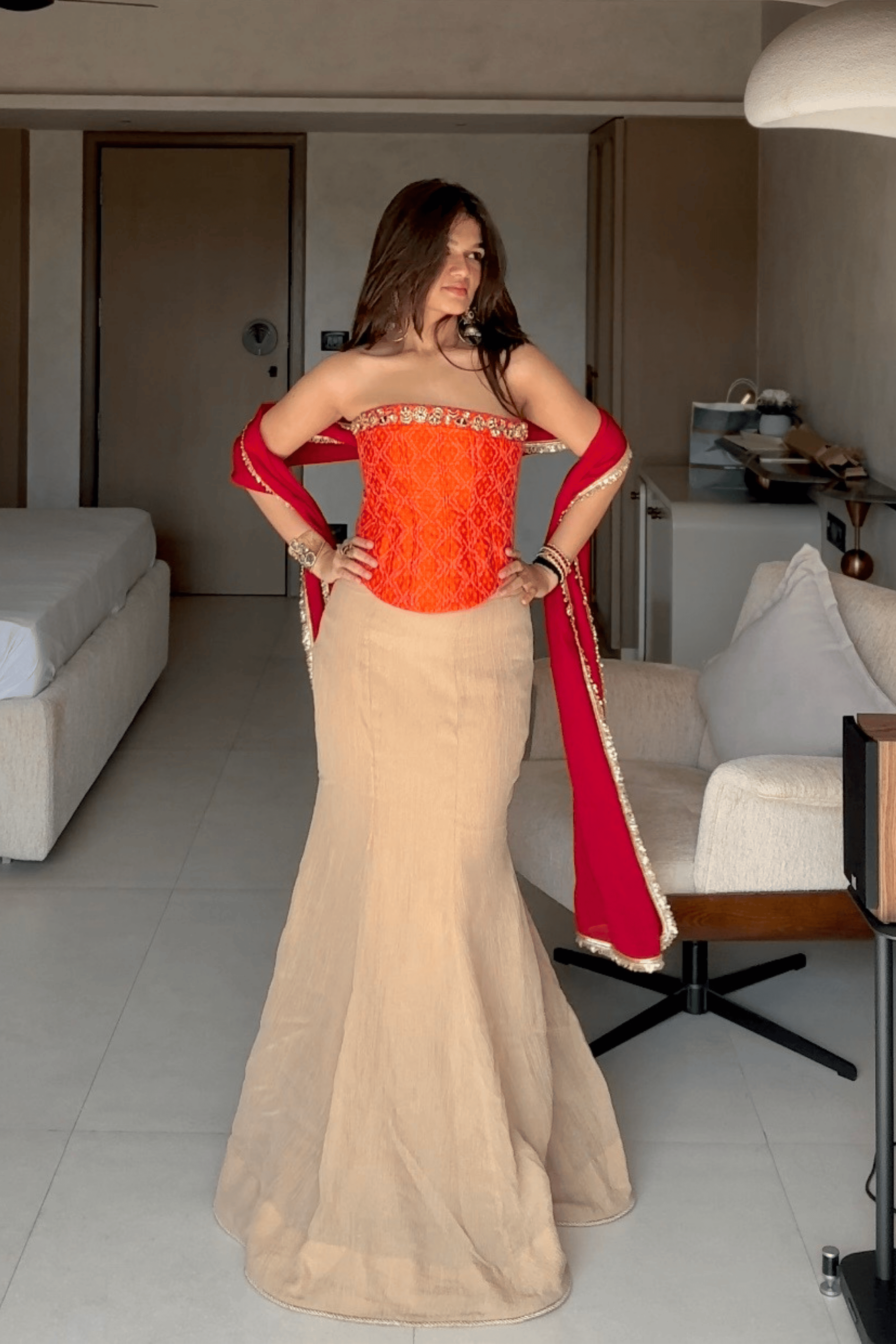 Woman in a red and beige traditional outfit standing in a living room.
